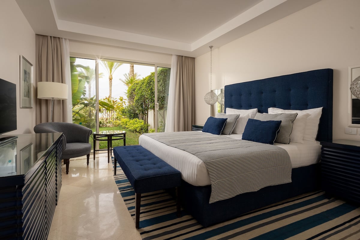 A modern hotel room with a large bed, a desk, a chair, and a view of the outdoors.