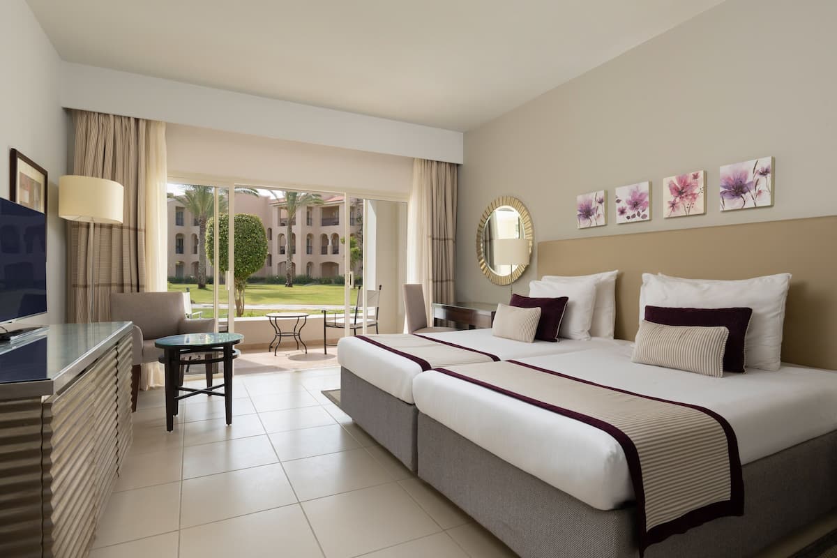A hotel room with a large bed, a desk, a chair, and a view of the courtyard.