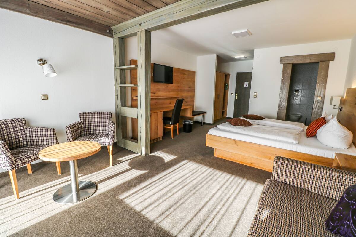 Ein Zimmer mit einem Bett, zwei Stühlen, einem kleinen Tisch, einem Fernseher und einem Holztisch.