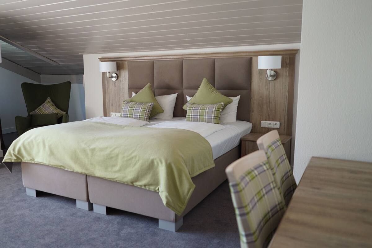 Ein Hotelzimmer mit einem großen Bett, zwei Nachttischen, einem Sessel und einer Lampe.