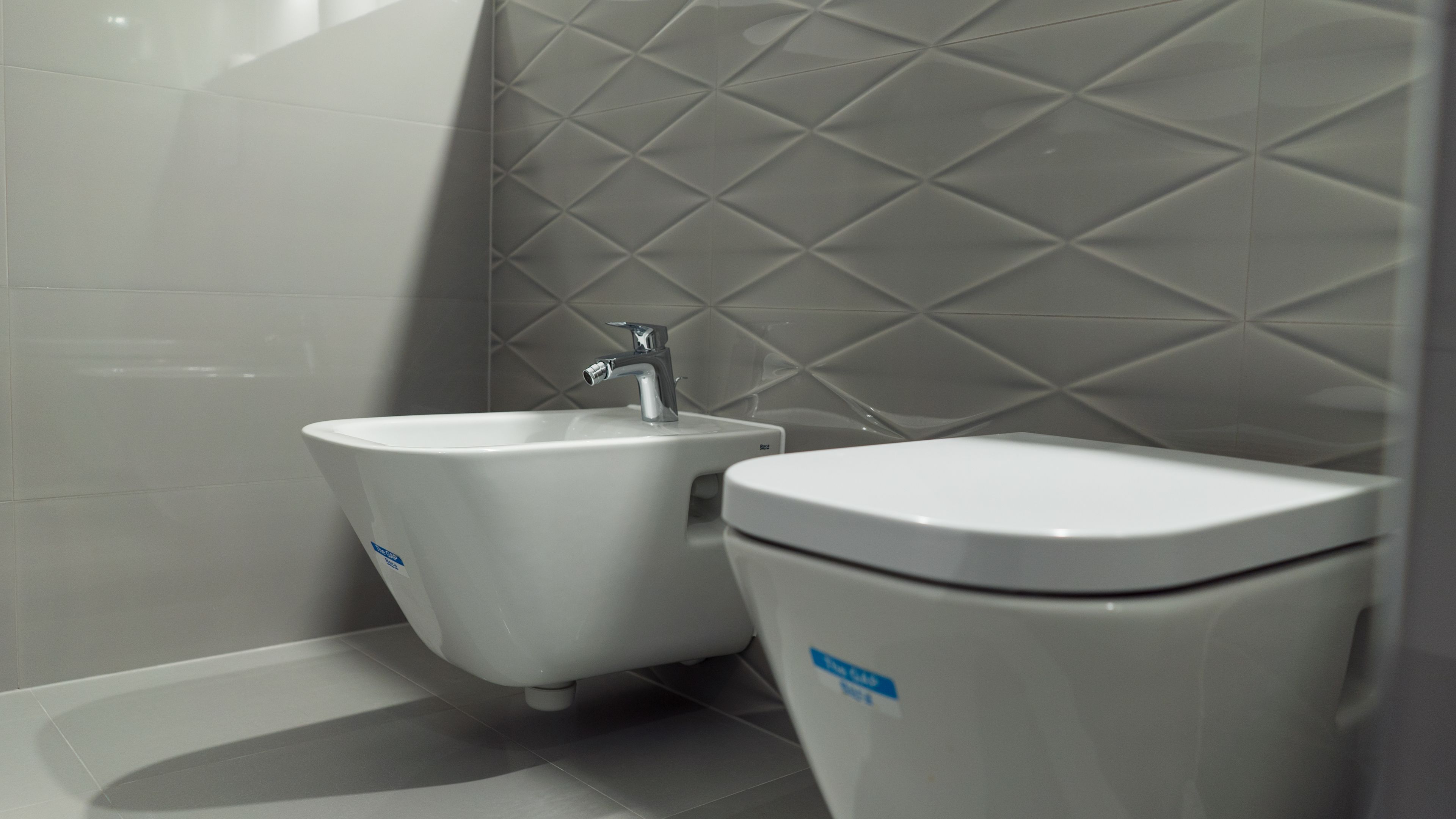A bathroom with a bidet, a toilet, and a wall with a diamond pattern.