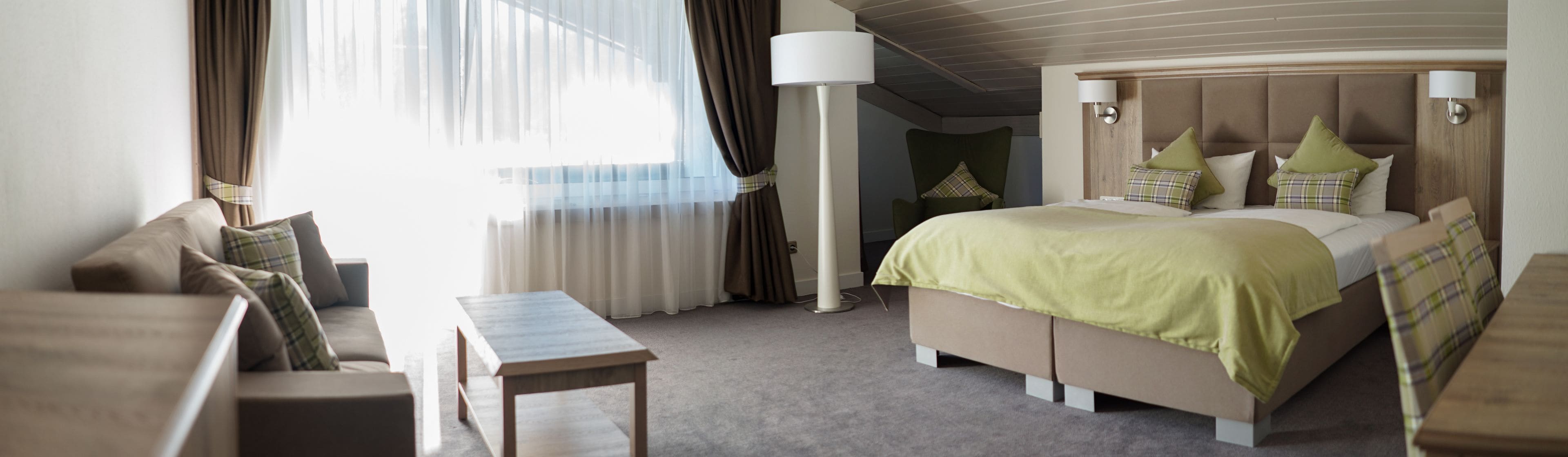 A hotel room with a bed, a sofa, a table, and a lamp.