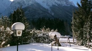 A snow-covered outdoor area with a wooden play structure and a snow-covered lamp post.