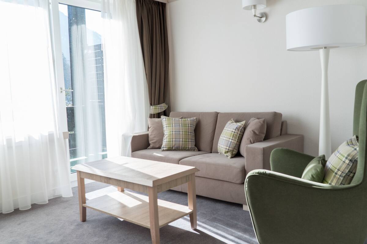 Ein modernes Wohnzimmer mit einer Couch, einem grünen Sessel, einem Holztisch und einer Stehlampe.