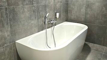 A modern bathroom with a freestanding bathtub, a handheld showerhead, and a wall-mounted faucet.