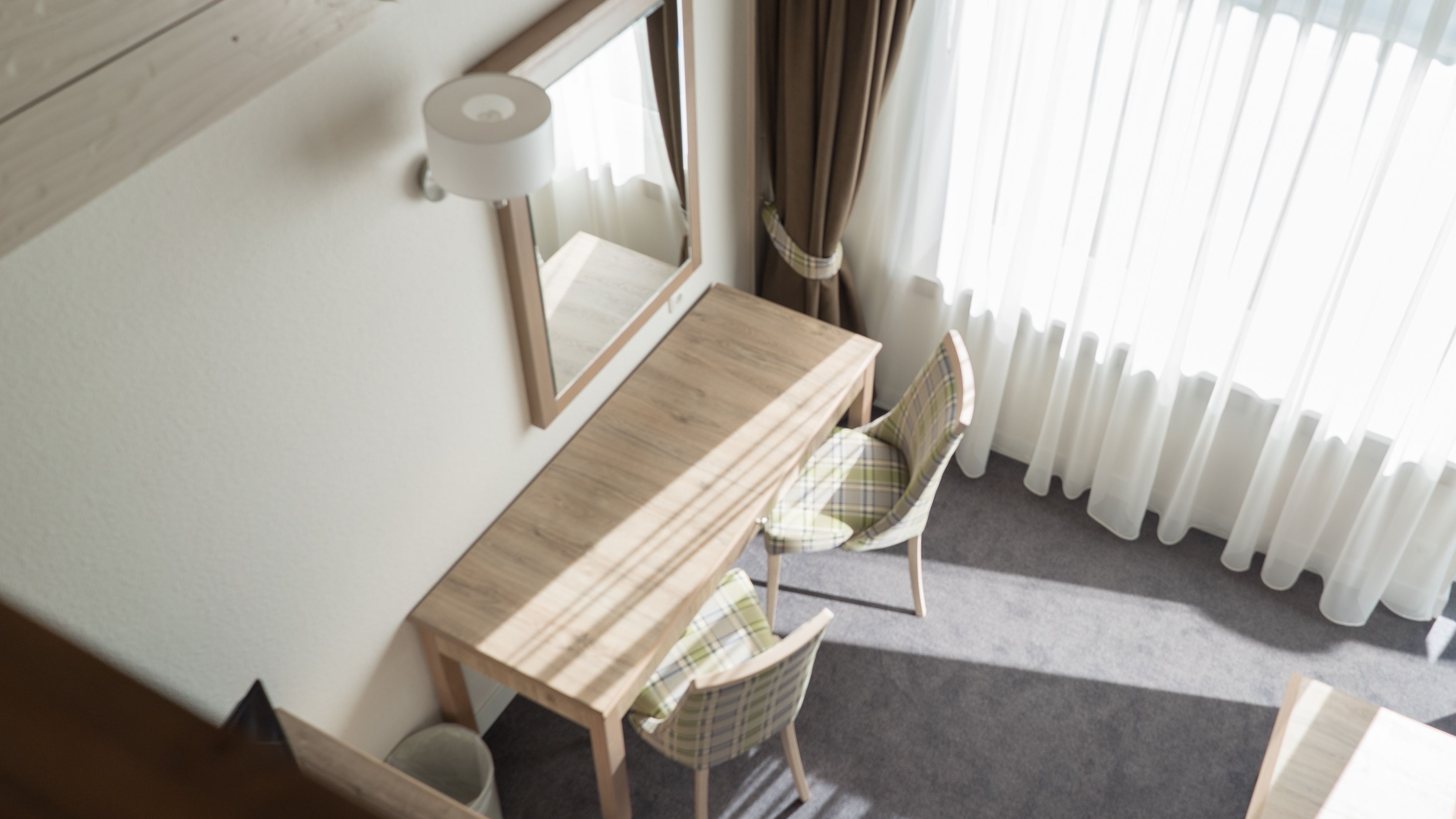 Una habitación con un escritorio de madera, dos sillas, un espejo y un radiador.