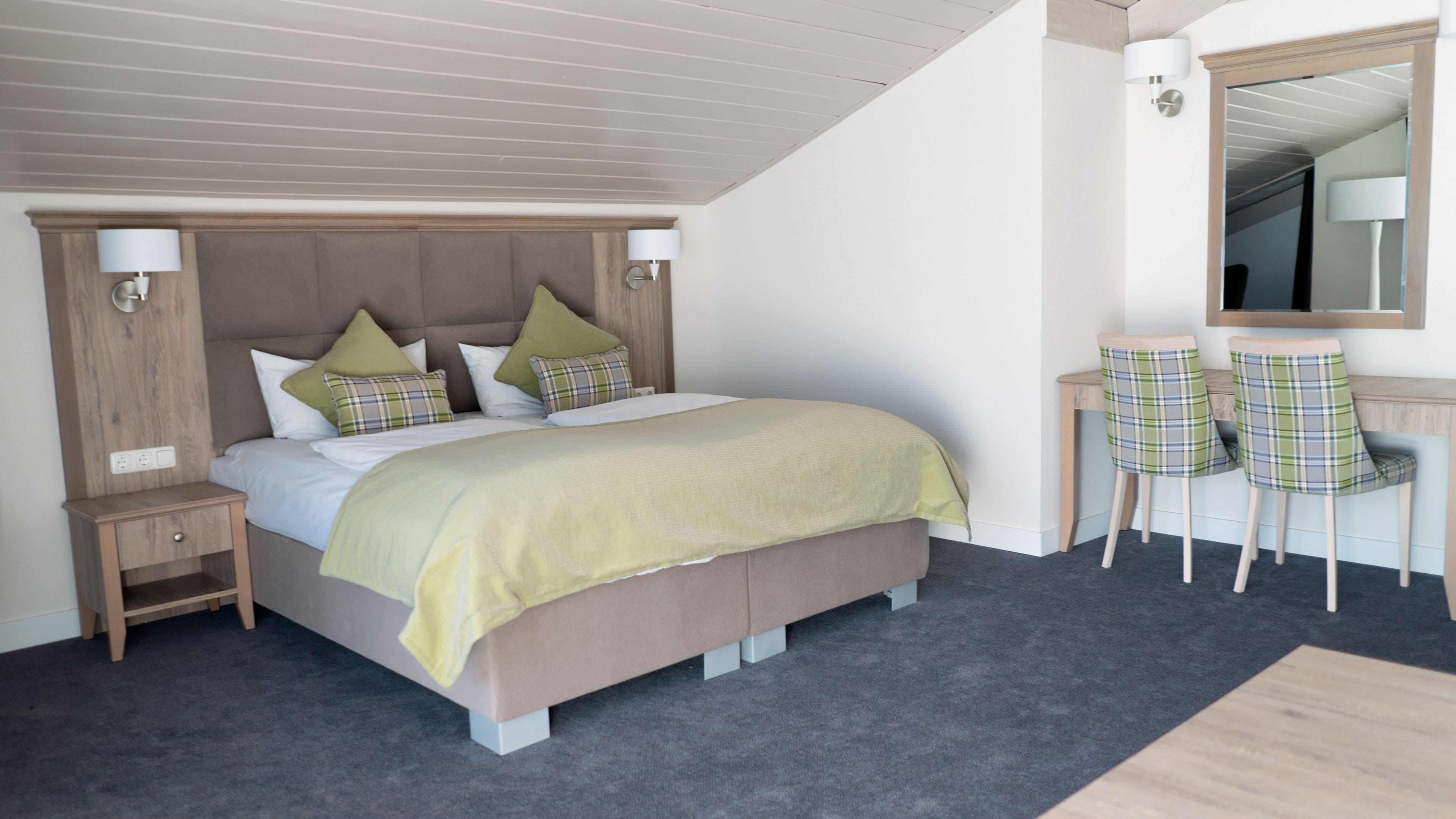 A bedroom with a bed, nightstands, a desk with chairs, and a mirror.