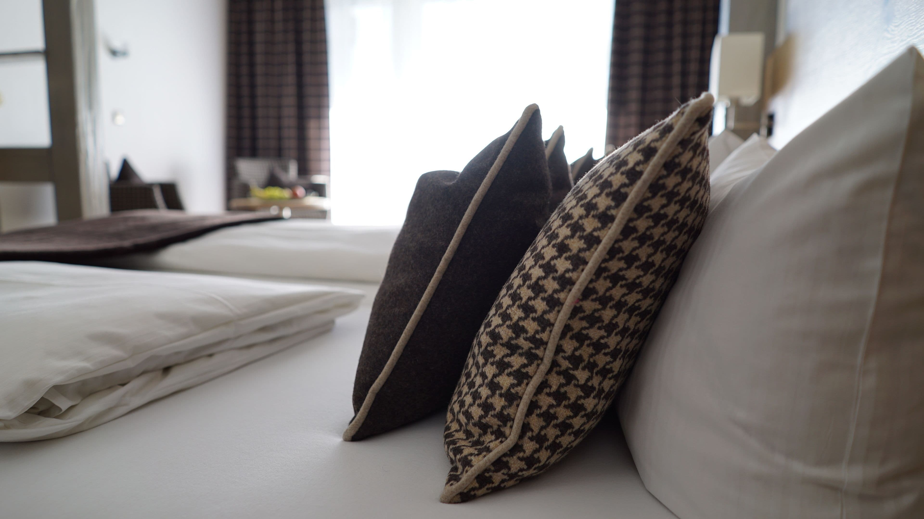 Un lit bien fait, avec du linge de lit blanc et deux coussins à motifs.