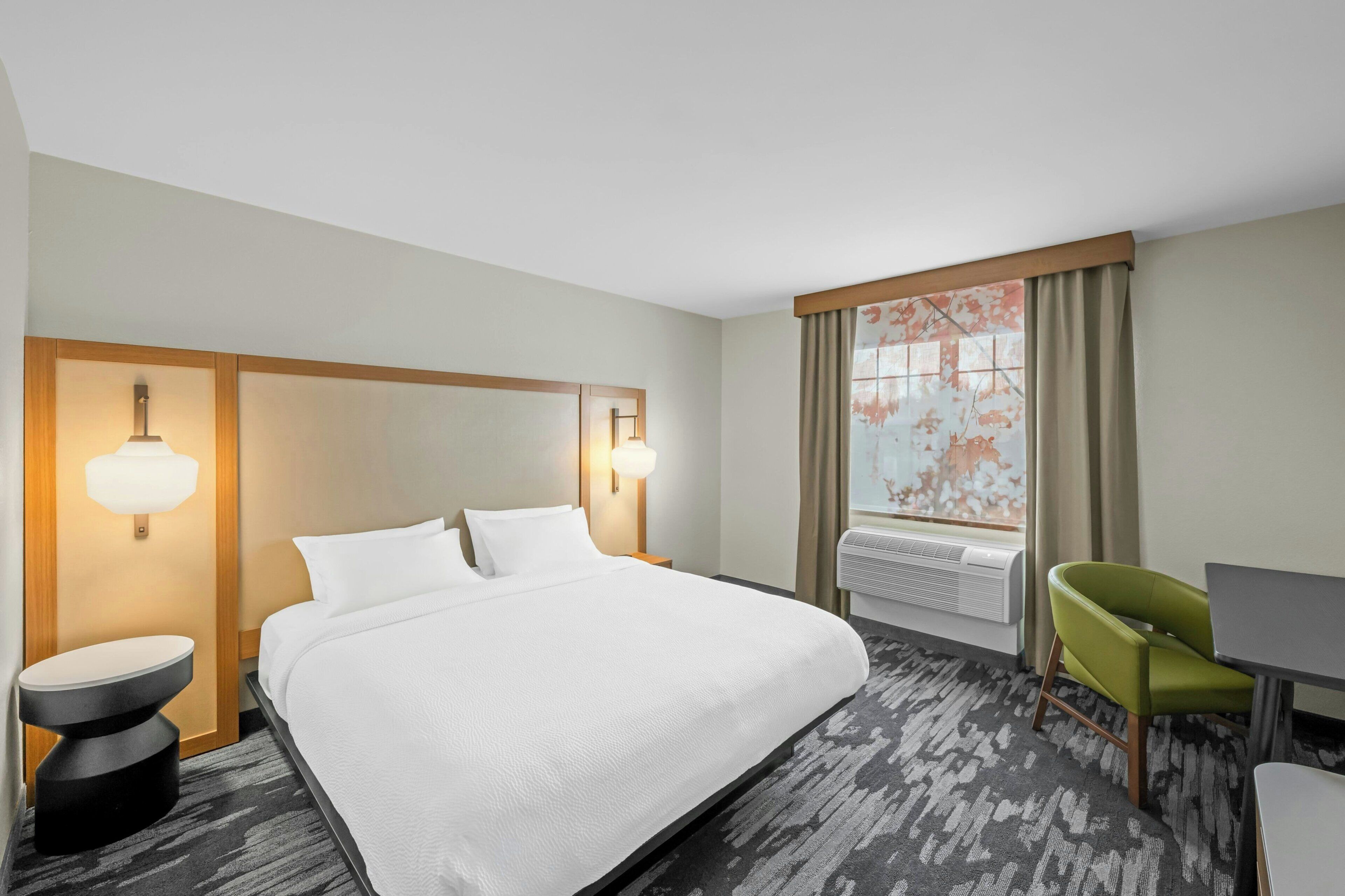 A hotel room with a large bed, bedside lamps, a desk, a chair, and a window with curtains.