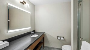 A modern bathroom with a large mirror, a sink, a toilet, and a glass shower enclosure.