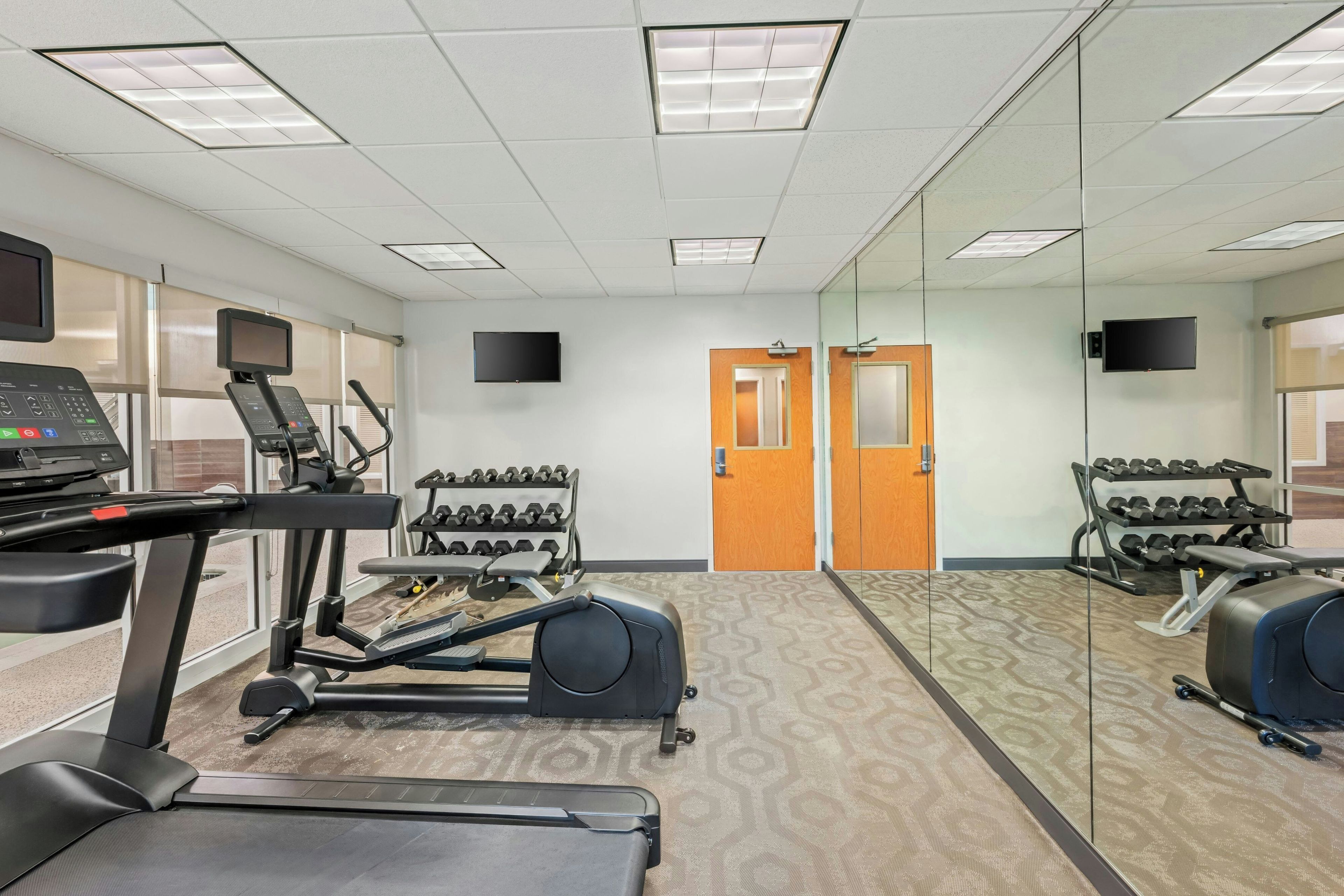 Un gimnasio con cintas de correr, una bicicleta estática y una pared de espejos.