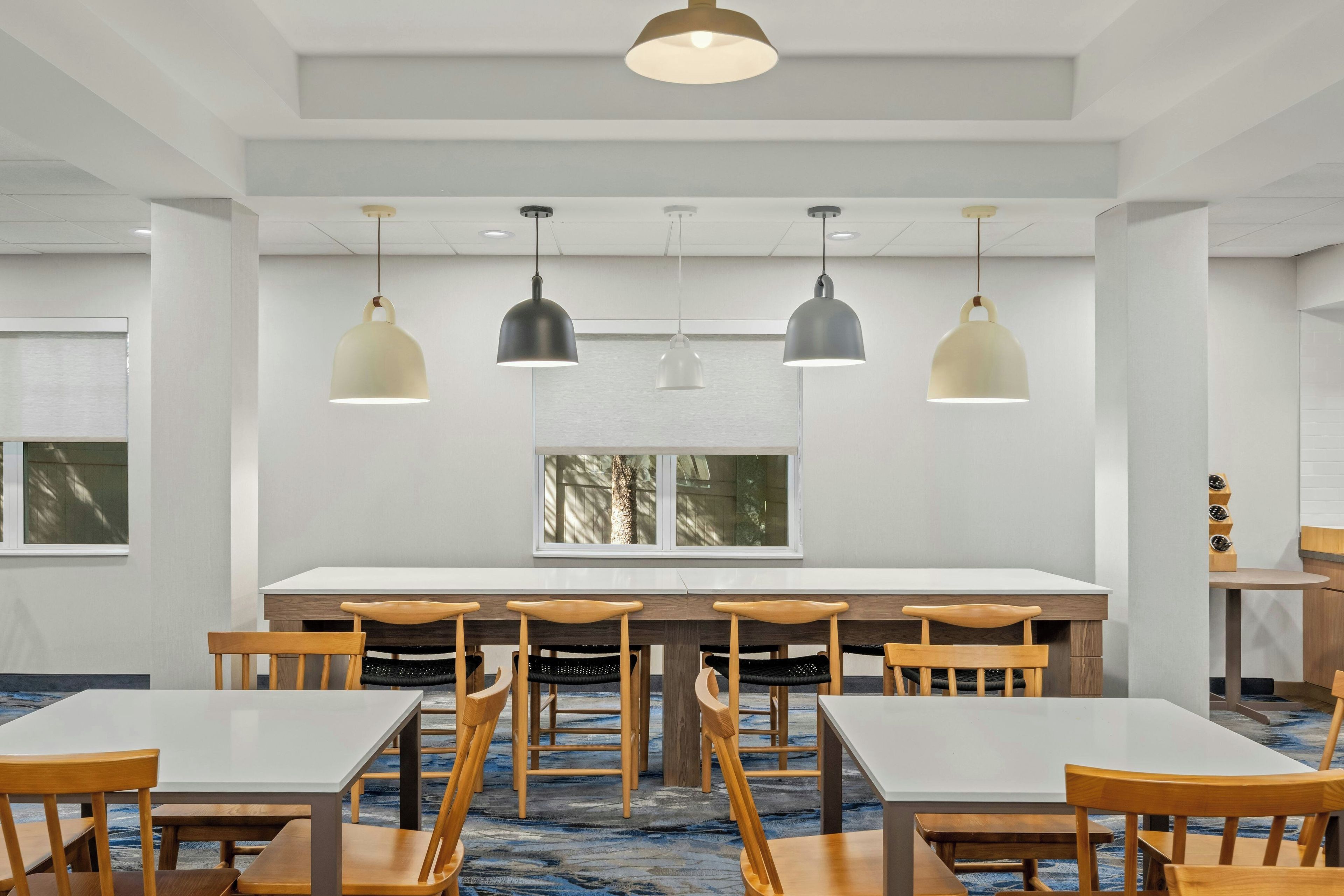 A conference room with a long table, multiple chairs, pendant lighting, and a window with a view of trees.