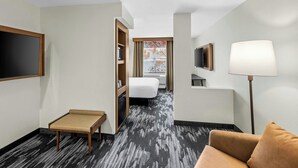 A hotel room with a bed, a desk, a chair, a TV, and a lamp.