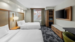 Habitación de hotel con dos camas, un escritorio, una silla, un televisor y una ventana con cortinas.