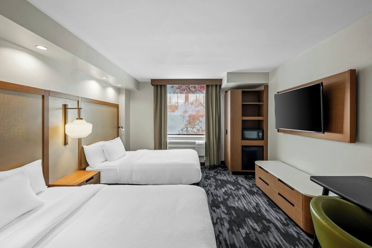 Une chambre d’hôtel avec deux lits, un bureau, une chaise, une télévision et une fenêtre avec des rideaux.