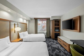Een hotelkamer met twee bedden, een bureau, een stoel, een televisie en een raam met gordijnen.