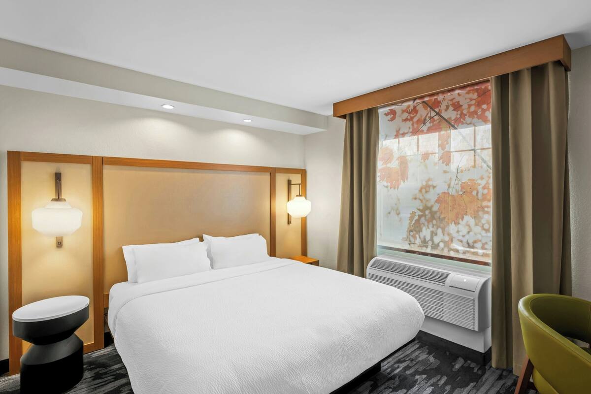 Une chambre d’hôtel avec un grand lit, deux lampes de chevet, une fenêtre avec des rideaux et un climatiseur fixé au mur.