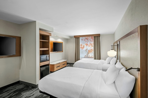 A hotel room with two beds, a TV, a desk with a microwave, and a window with a view.