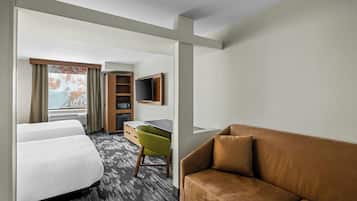 A hotel room with two beds, a desk, a green chair, a brown sofa, and a TV mounted on the wall.