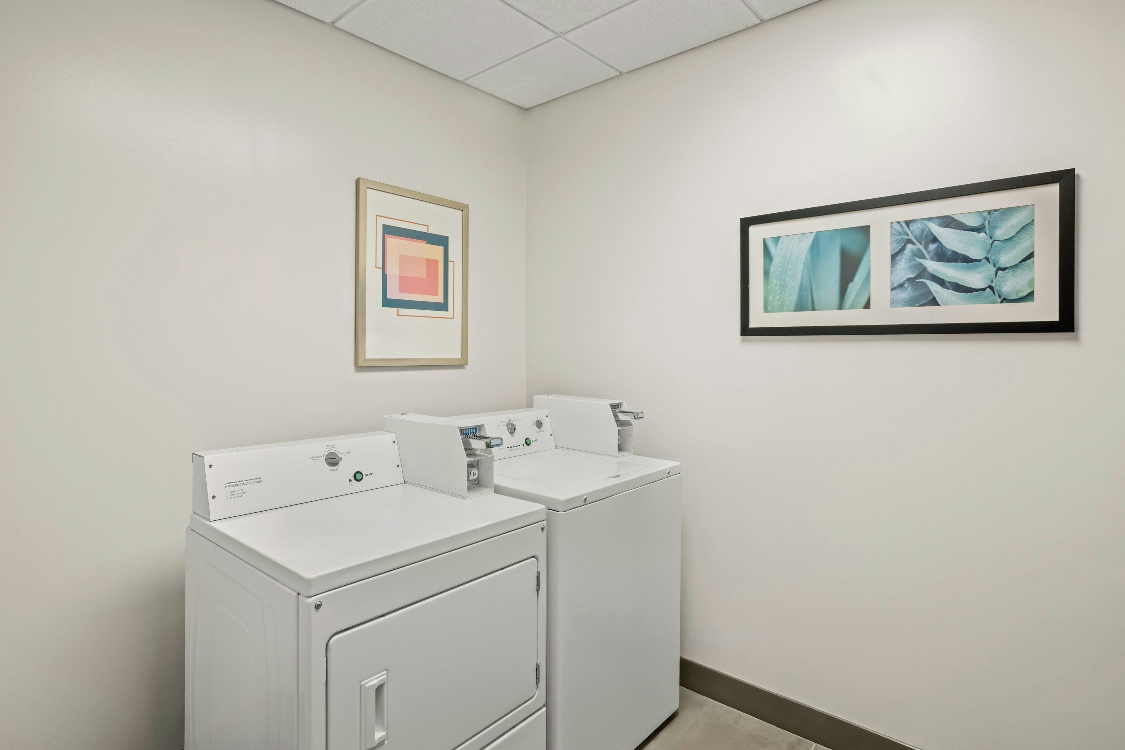A laundry room with two white washing machines and two framed artworks on the wall.