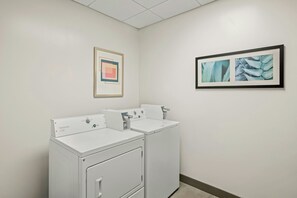 Une buanderie avec deux machines à laver blanches et deux œuvres d’art encadrées accrochées au mur.