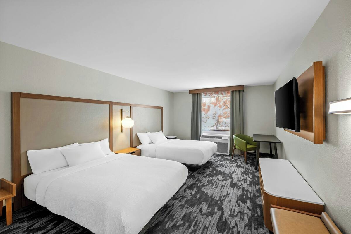 Une chambre d’hôtel avec deux lits, un bureau, une chaise, une télévision et une fenêtre avec des rideaux.