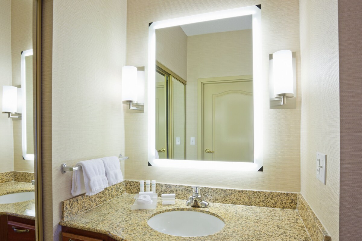 A bathroom with a granite countertop, a sink, a mirror, and a towel rack.