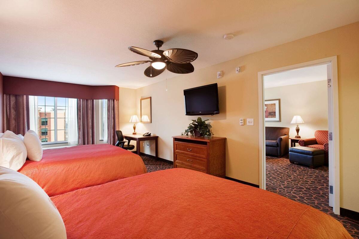A hotel room with two beds, a desk, a television, and a view of the cityscape.