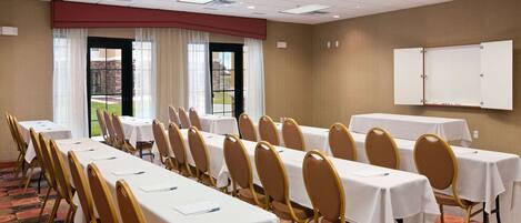 A conference room with long tables and chairs, a whiteboard, and a view of the outdoors through large windows.