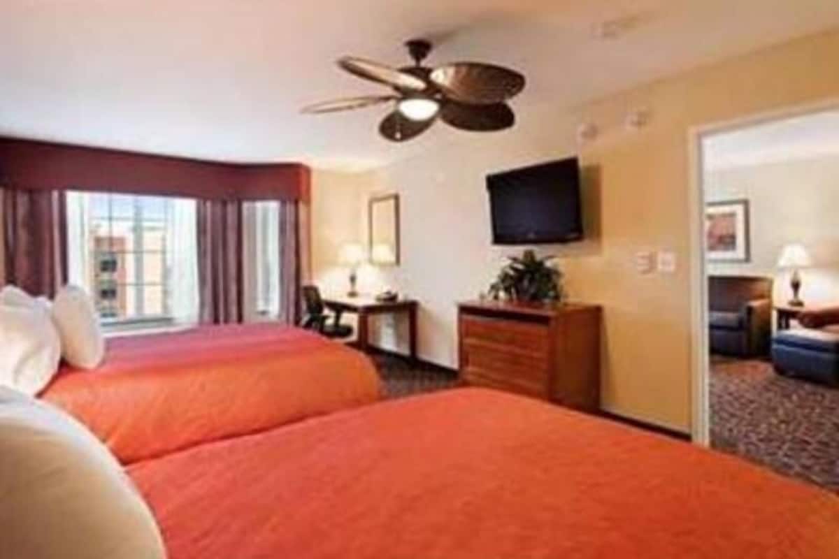 A hotel room with two beds, a ceiling fan, a TV, and a desk with a lamp.