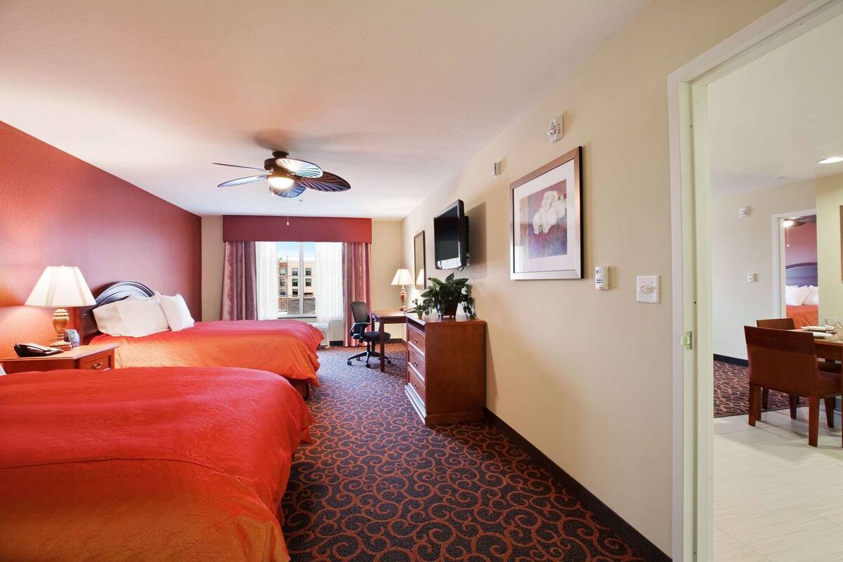 A hotel room with two beds, a desk, a chair, a television, and a window with curtains.