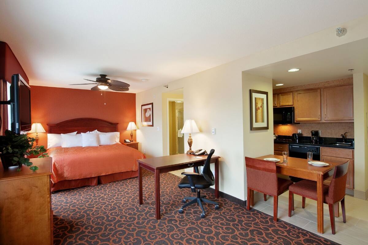 A hotel room with a bed, desk, chairs, and a kitchenette.