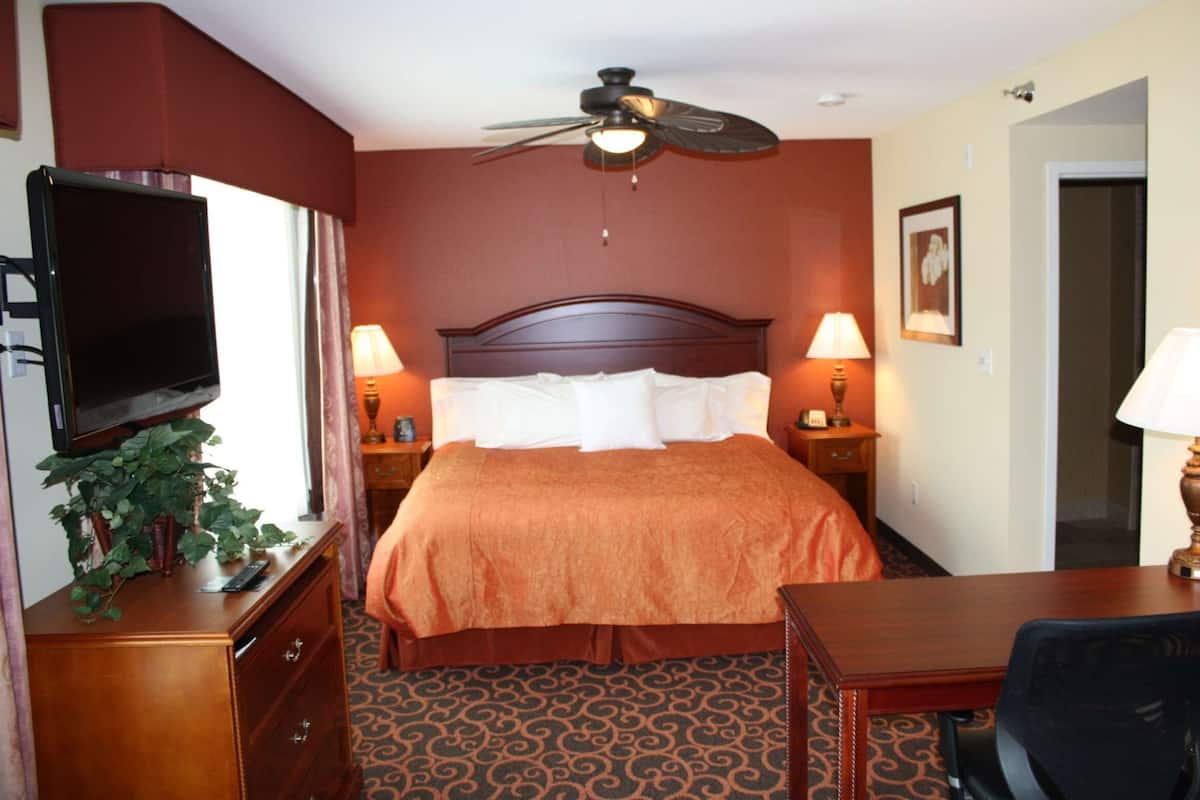 A hotel room with a large bed, two bedside lamps, a ceiling fan, a TV on a dresser, and a desk with a chair.
