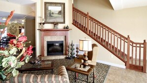A spacious living room with a fireplace, a staircase, and a view of the outdoors. - GrandStay Residential Suites Hotel (Faribault)