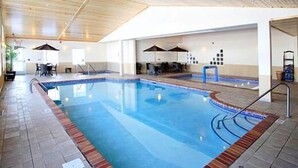 An indoor swimming pool with a tiled floor, a blue pool edge, and a wooden ceiling. - GrandStay Residential Suites Hotel (Faribault)