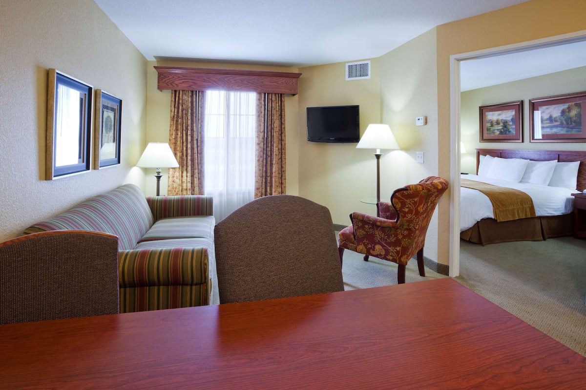 A hotel room with a bed, a sofa, a dining table, and two armchairs.