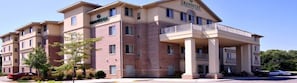 A multi-story hotel with a brick facade, a covered entrance with columns, and a sign reading "GrandStay".