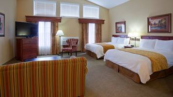 A hotel room with two beds, a TV, a desk, a chair, and a window with blinds.