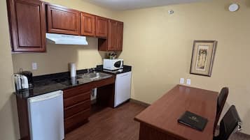 Cocina compacta con armarios de madera, microondas, lavamanos y un refrigerador pequeño.