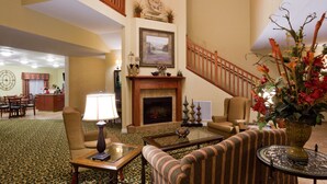 A spacious lobby with a fireplace, striped armchairs, a coffee table, and a dining area in the background. - GrandStay Residential Suites Hotel (Faribault)