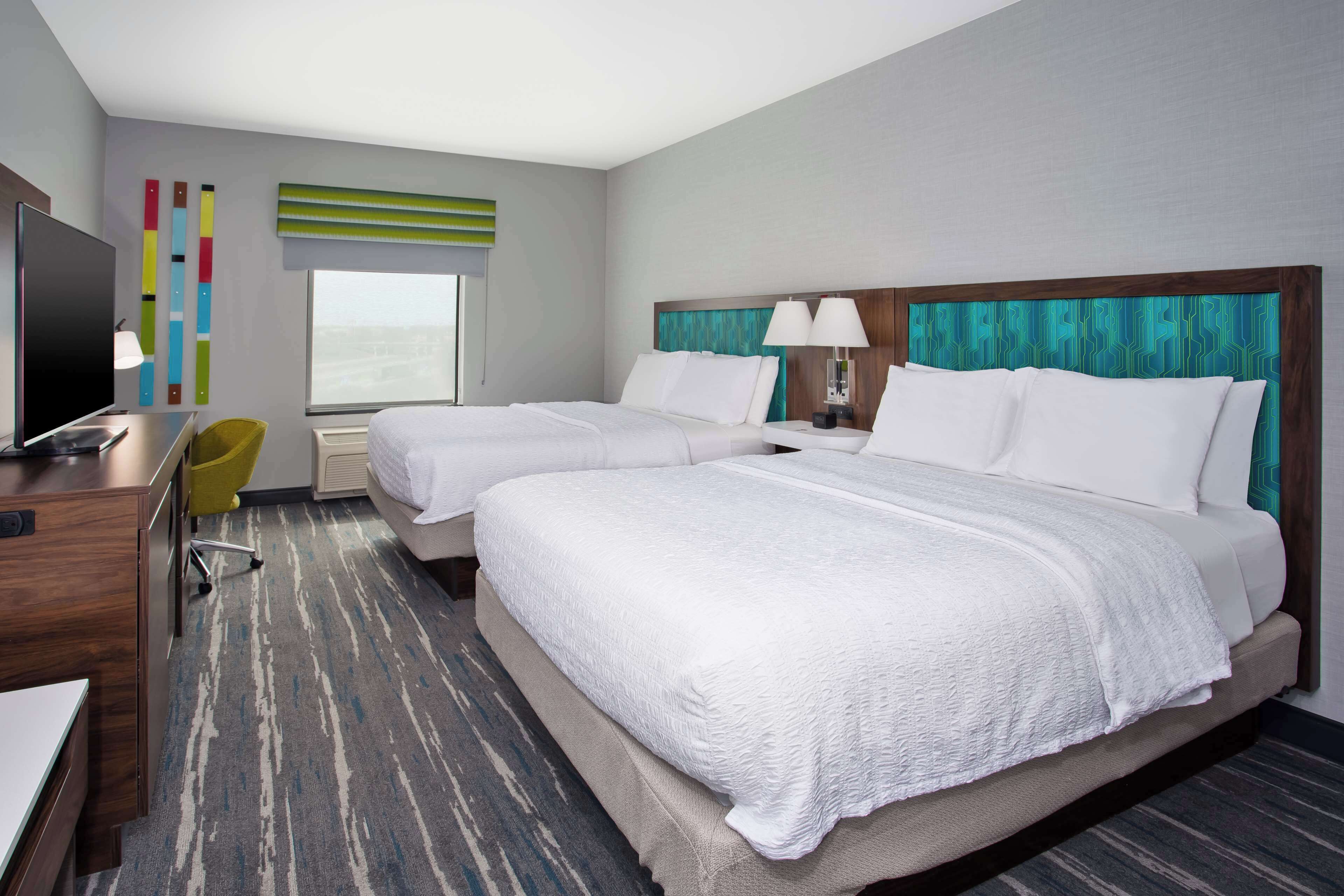 A hotel room with two beds, a desk, a chair, a TV, and a window with a view.