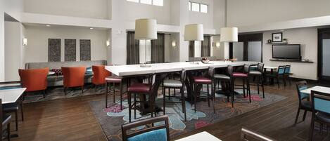 A spacious hotel dining area with high ceilings, multiple tables and chairs, and large windows allowing natural light.