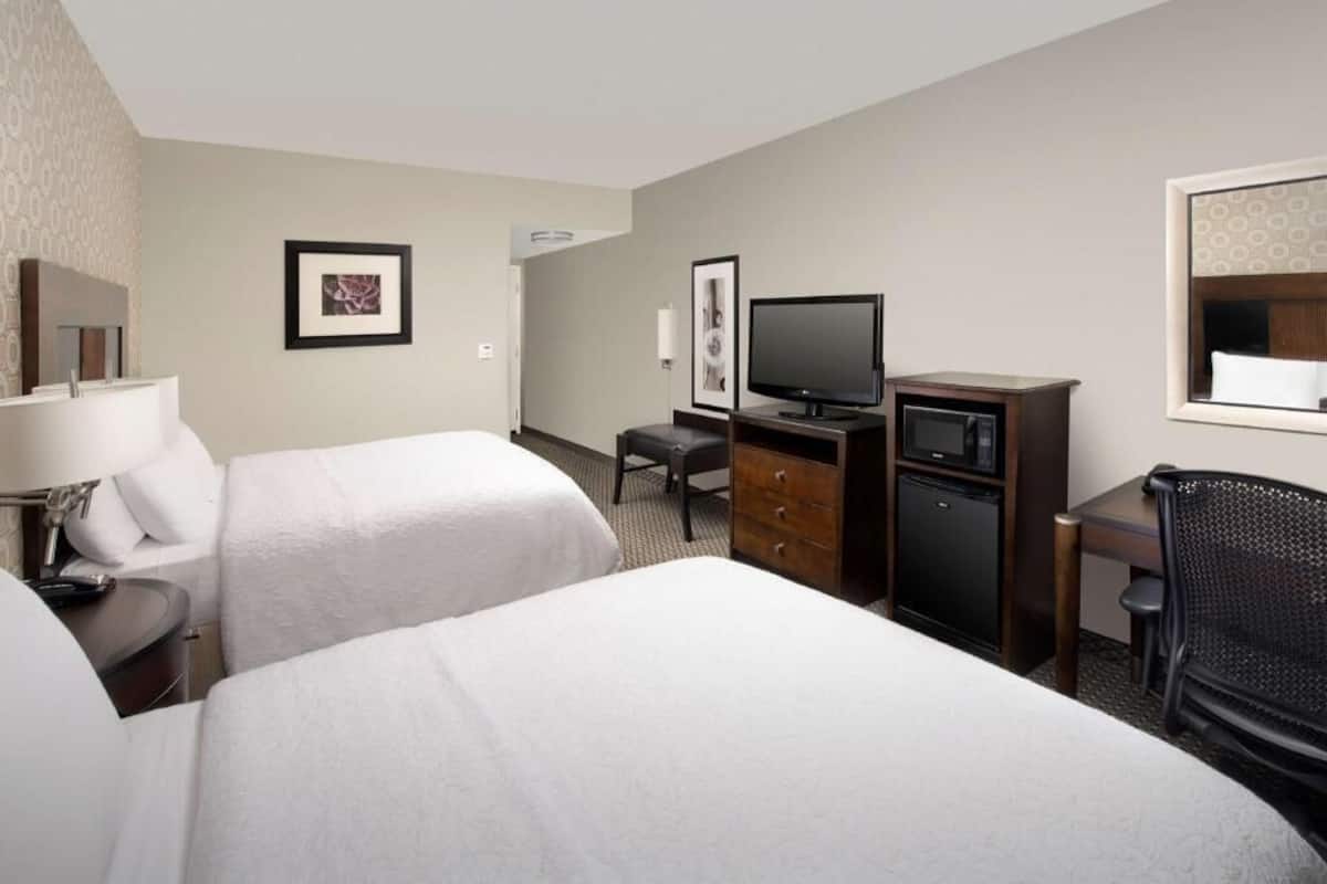 A hotel room with two beds, a desk with a computer, a television, a chair, and a small cabinet.