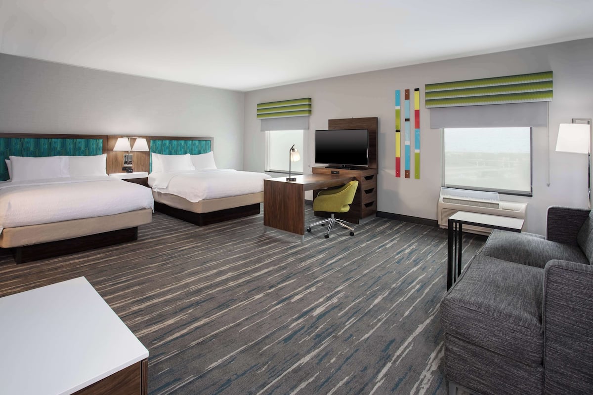 A hotel room with two beds, a desk with a chair, a TV, and a large window.