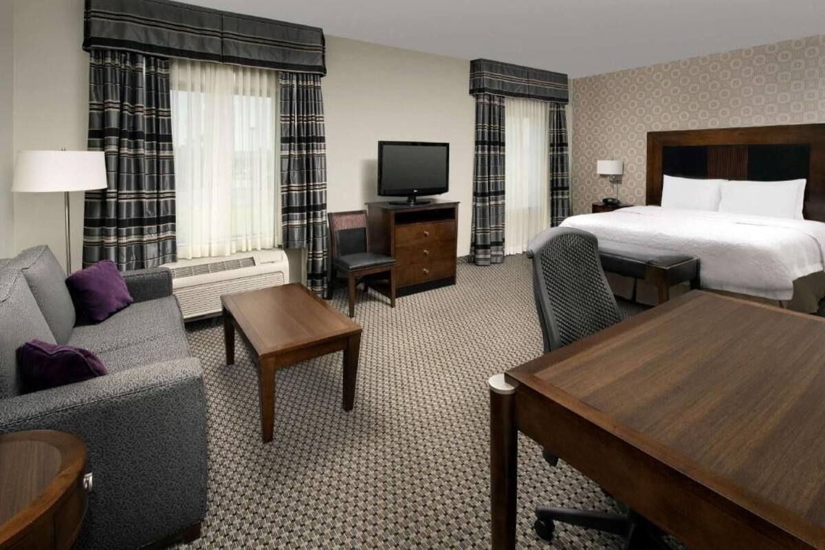 A hotel room with a bed, a TV, a sofa, a desk, and a chair.