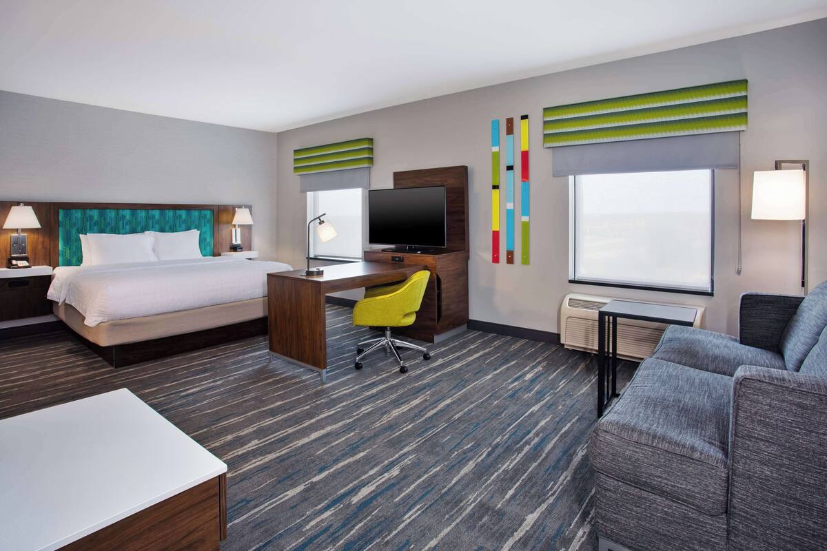 A hotel room with a bed, desk, chair, TV, and a sofa.