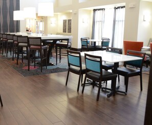 A hotel dining area with multiple tables and chairs, a patterned rug, and a large window with curtains. - Hampton Inn & Suites Athens-I-65 (Huntsville Area) (Athens)