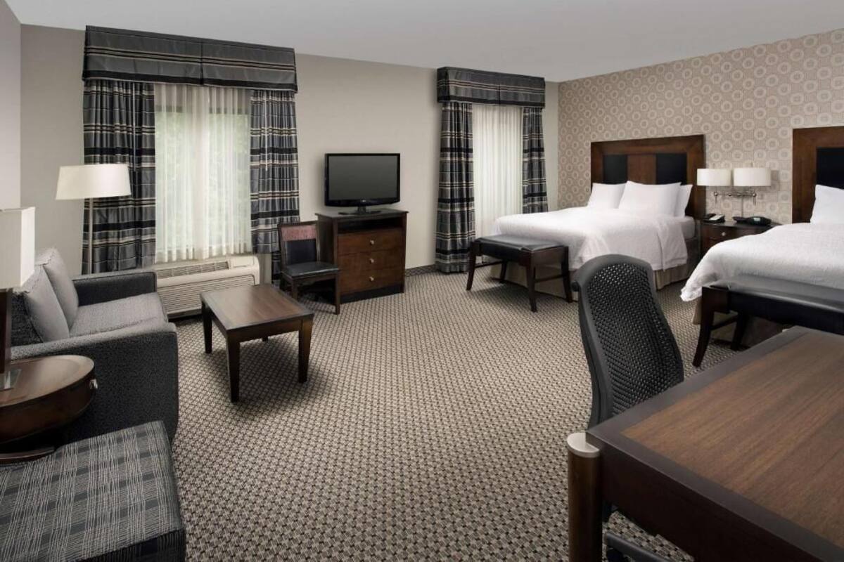 A hotel room with a bed, two bedside tables, a TV, a sofa, a chair, and a desk.