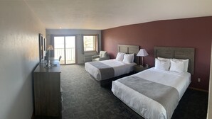 Ein Hotelzimmer mit zwei Betten, einem Schreibtisch, einem Stuhl, einem Fernseher und einem Fenster mit Vorhängen.