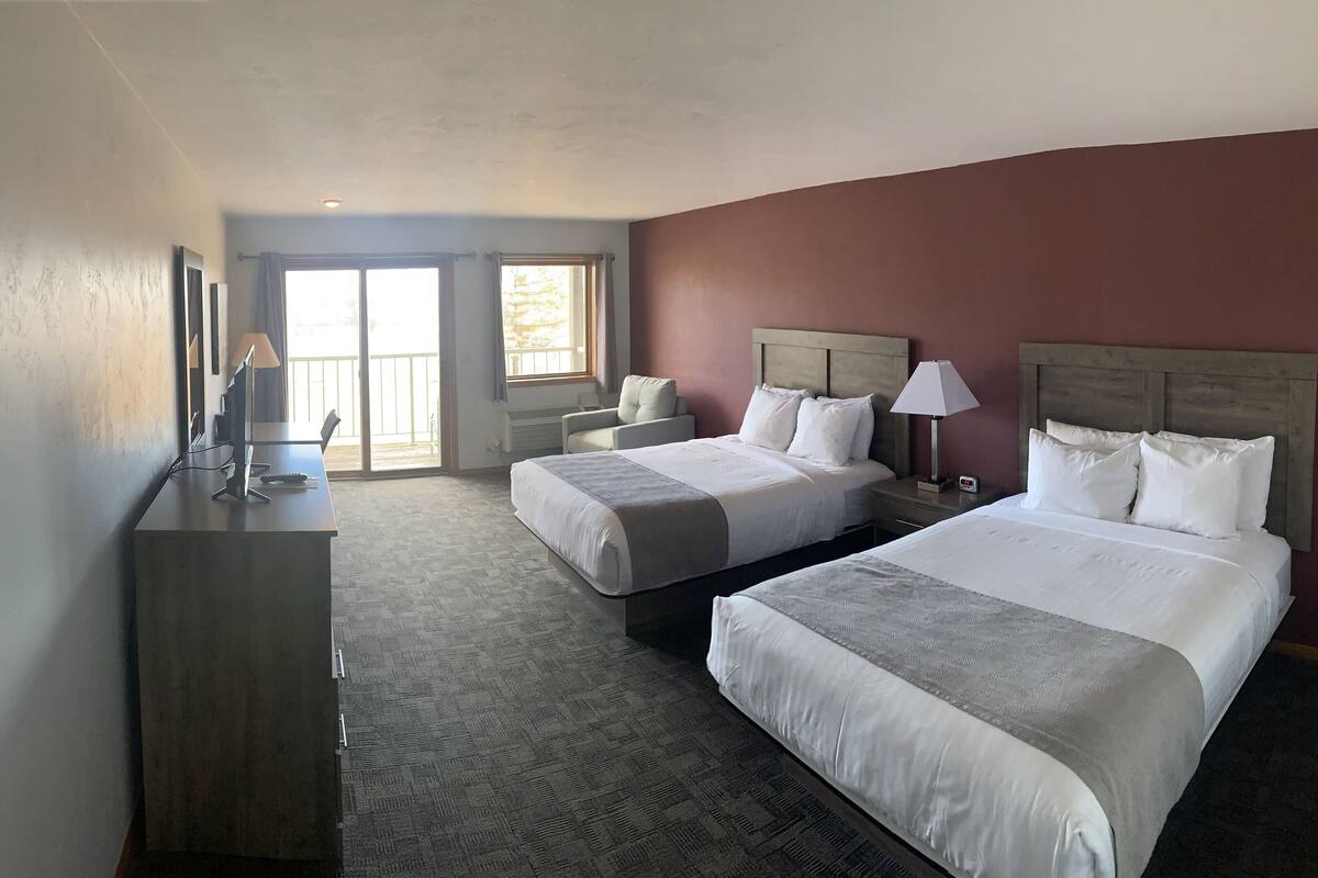 A hotel room with two beds, a desk, a chair, a TV, and a window with curtains.